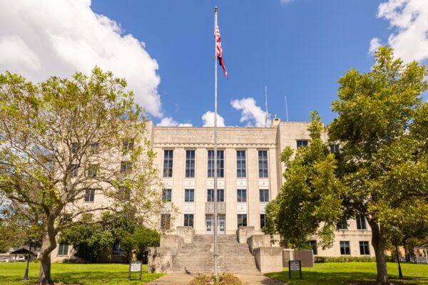 Brazoria County Courthouse in Angleton, Texas. A tan strone 5 story building with a large staircase entrance and windows all around the structure.