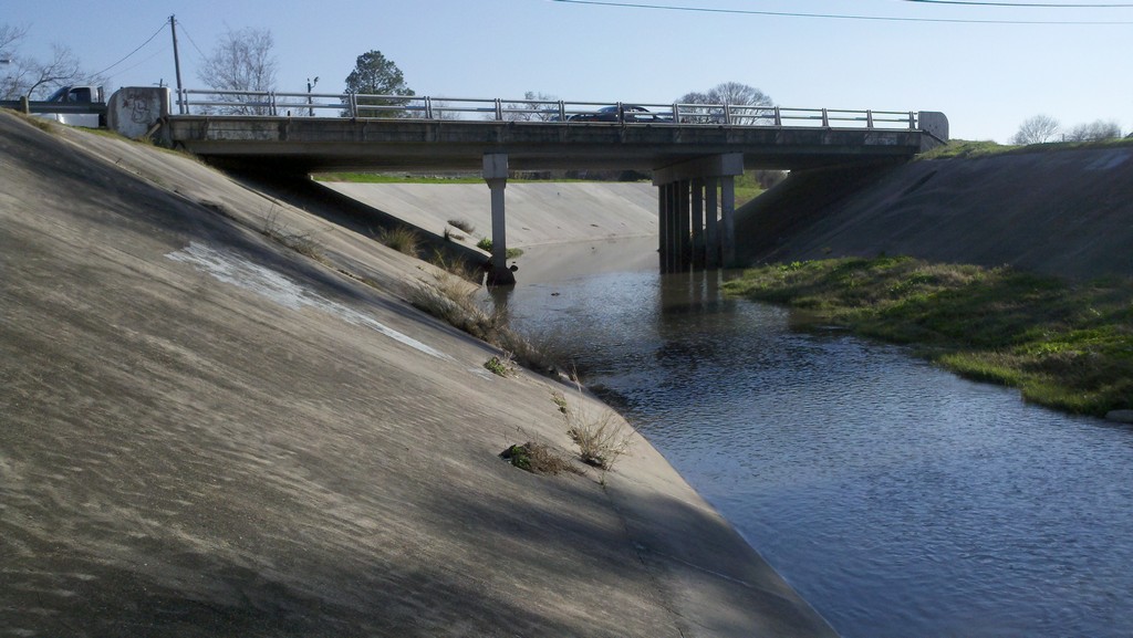 concrete drainage bayou running under a roadway bridge