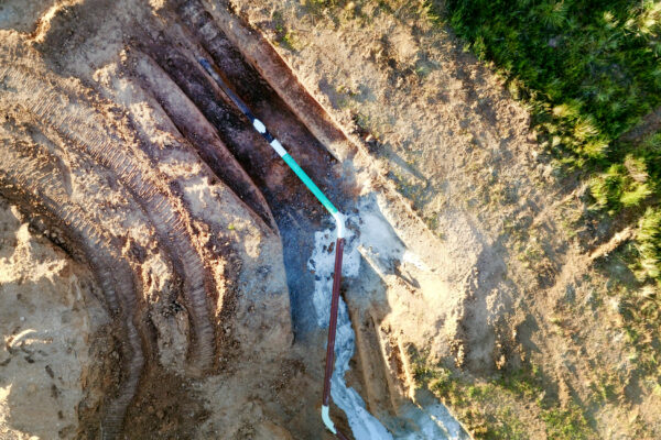 aerial view of an exposed teal and white pipeline in dirt