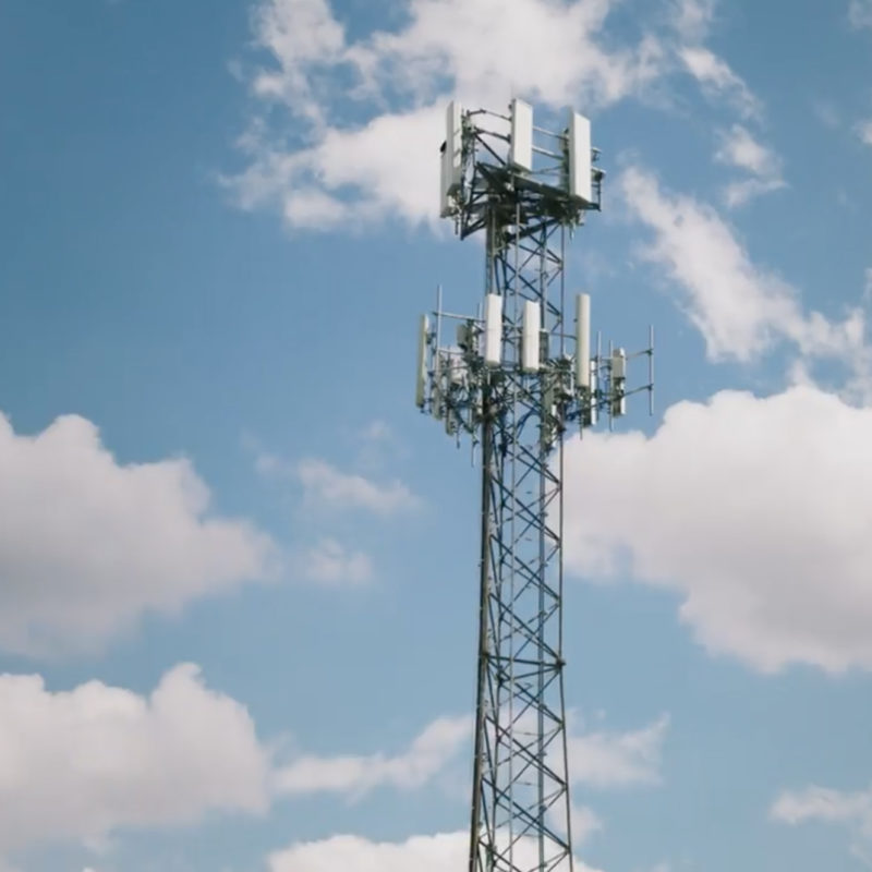 Looking up at top of radio tower with blue sky and clouds in the background.