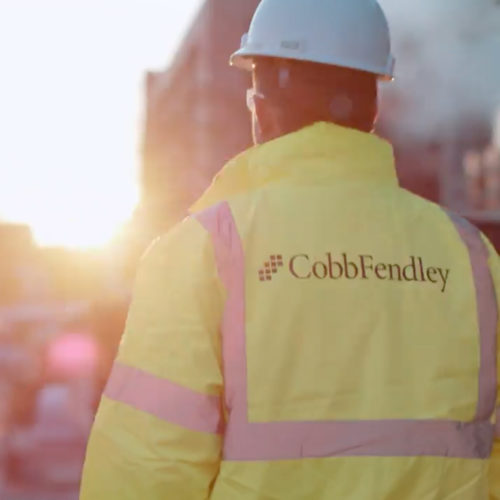 Construction worker walking away from camera with yellow CobbFendley jacket.