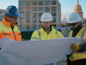 3 CobbFendley employees looking at a plan set in front of a building. All wearing hard hats and yellow safety vests.